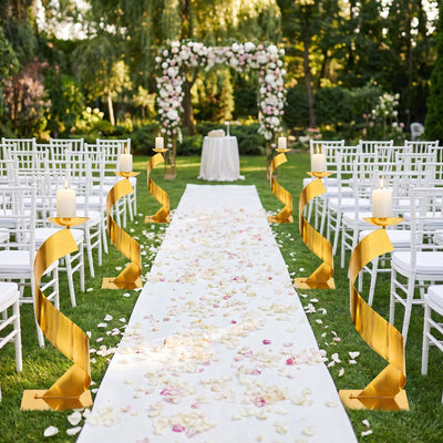 Elegant outdoor wedding aisle with white chairs, gold candle stands, and floral arch