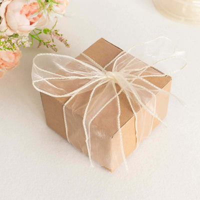 Brown gift box tied with a sheer ribbon, surrounded by soft flowers.