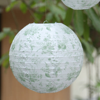 Floral paper lantern hanging in a garden setting.