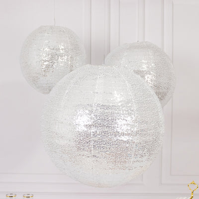 Three shimmering silver decorative lanterns hanging against a plain backdrop.