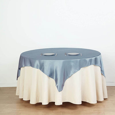 Round table with blue satin tablecloth and white skirt, set with plates and utensils.