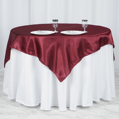 Burgundy satin tablecloth on a round white table with dinnerware