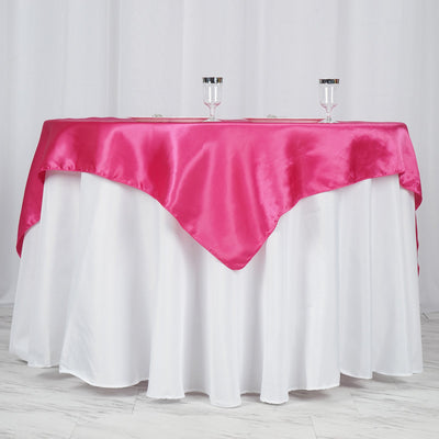 Pink satin tablecloth draped over a white table with two glasses on top.