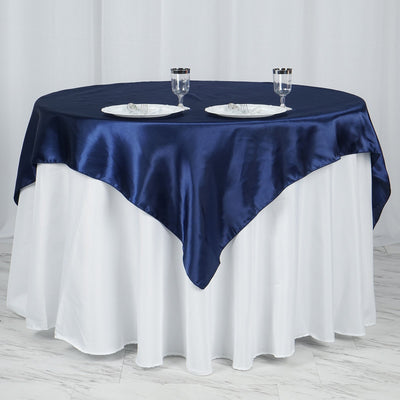 Navy satin tablecloth draping over a round white table with plates and glasses