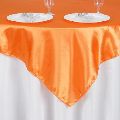 Orange satin tablecloth draping over a table with white plates and glasses.