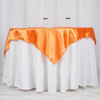 Orange satin table overlay on a white tablecloth with glasses.