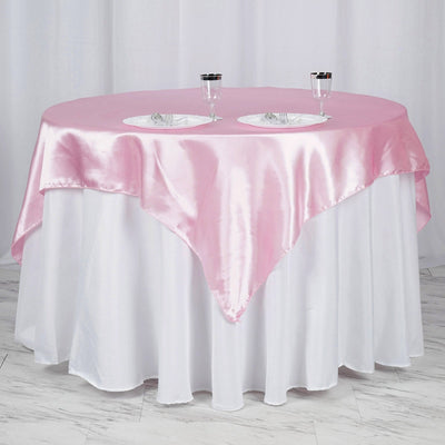 Pink satin tablecloth draped over a round table with plates and glasses.