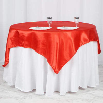 Round table with a red satin tablecloth and two empty plates.