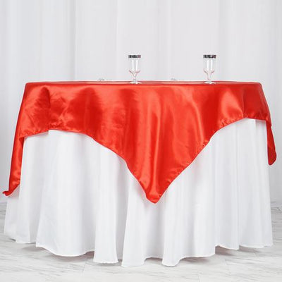 Red satin table cover draped over a round white table with glasses on top.