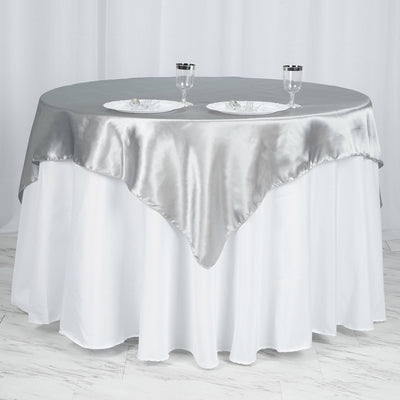 Elegant round table with silver satin tablecloth and two plates.