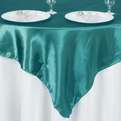 Teal satin tablecloth draped over a white table with plates and cutlery.