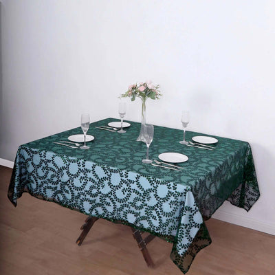 Elegant green floral tablecloth on a dining table with glassware and plates.