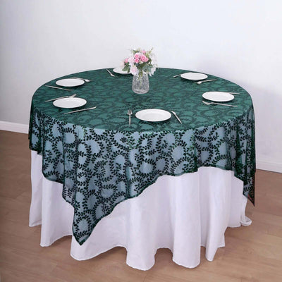Round green floral tablecloth on a white table with plates and a vase of flowers.