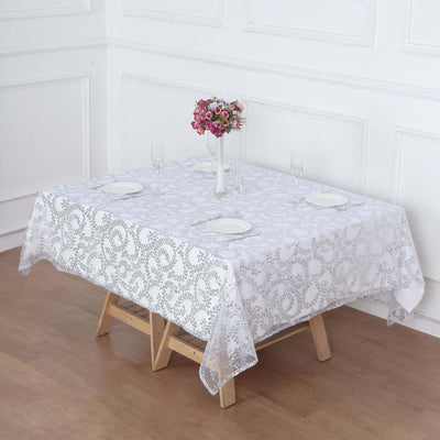 White lace tablecloth on a wooden table set for dining with flowers.