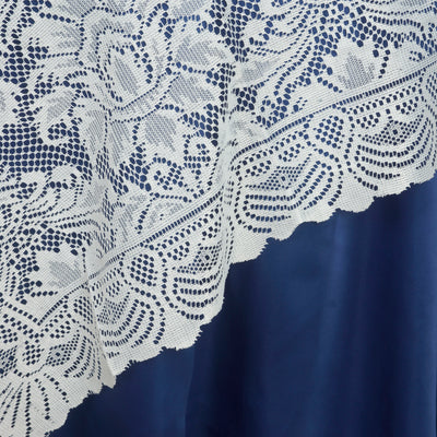 White lace tablecloth draped over blue fabric, showcasing intricate floral patterns.