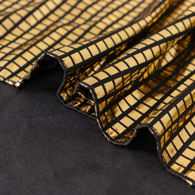 Gold patterned fabric with a grid design on a dark background.