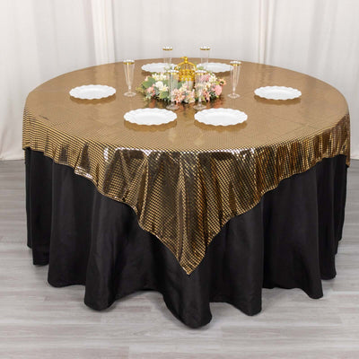 Gold sequin tablecloth on a round table set with plates and floral centerpiece.