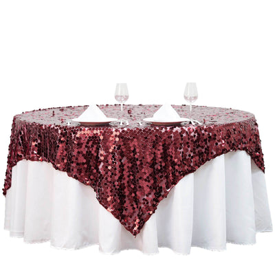 Burgundy sequin tablecloth draped over a round table with wine glasses.