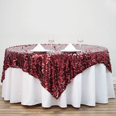 Burgundy sequin tablecloth draped over a round table with wine glasses and napkins.