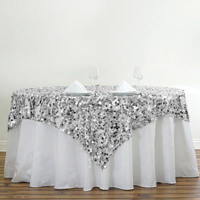 Silver sequin tablecloth draped over a round table with glassware and napkins.