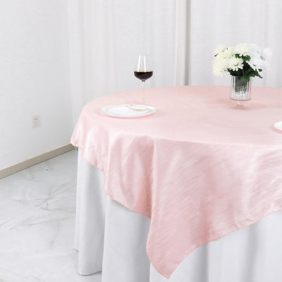 Elegant pink tablecloth draped over a round table with a wine glass and flowers.