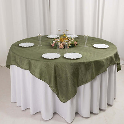 Round olive green tablecloth draped over a white table with plates and decor.