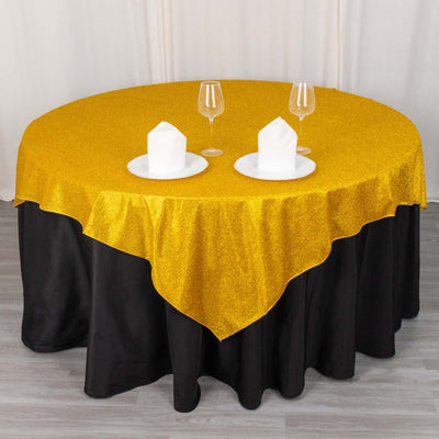 Gold glitter tablecloth on a round table with white plates and glasses.