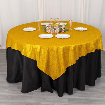 Gold glitter tablecloth draped over a round table with decorative plates and centerpieces.