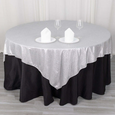 Round table with silver and black tablecloth, set with plates and glasses.