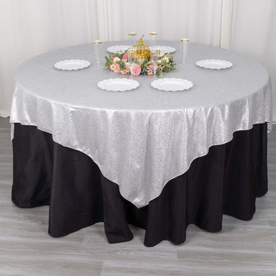 Round table set with a silver glitter tablecloth and decorative flowers.