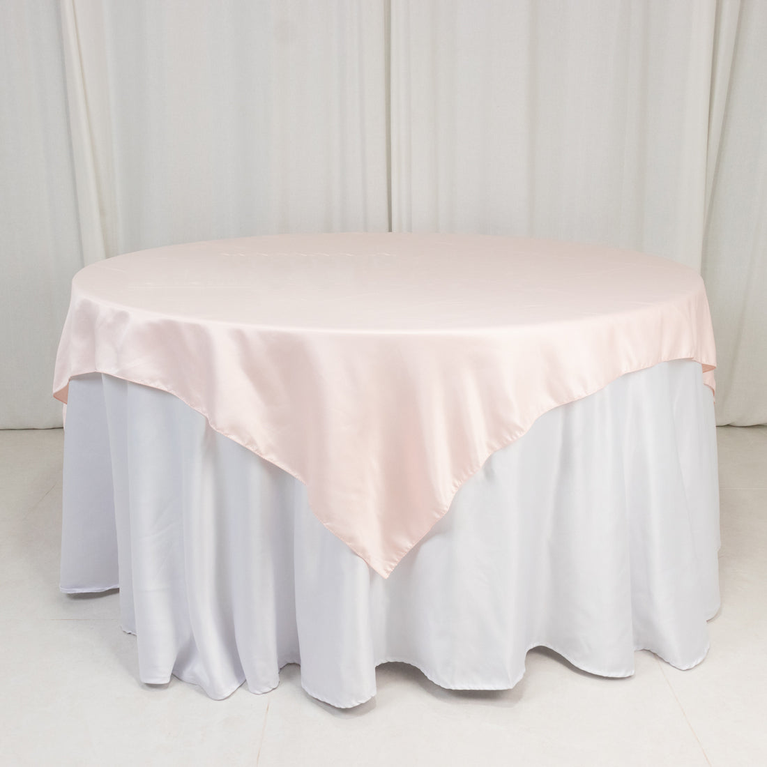 Round table with a pink satin tablecloth on a white skirt.