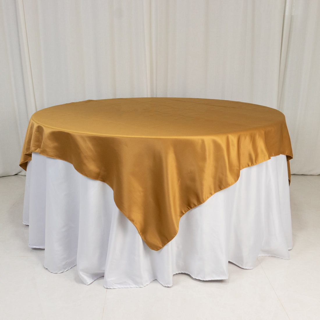 Round gold satin tablecloth on a white table.