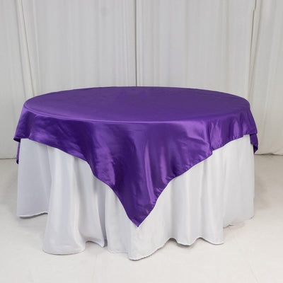 Round table with a purple satin tablecloth and white skirt.