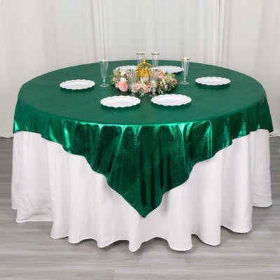 Green tablecloth draped over a round table with elegant decorations and plates.