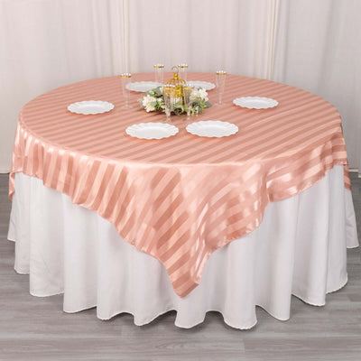 Round table dressed in a pink striped tablecloth with decorative plates.