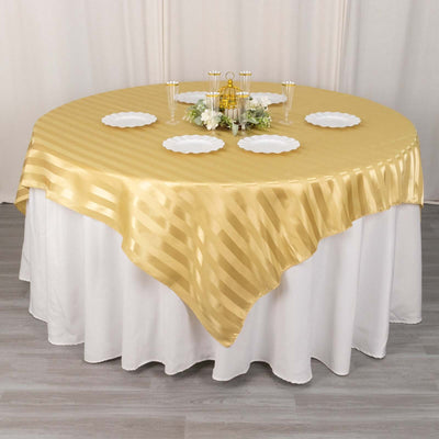 Gold striped tablecloth draped over a round table with white plates and décor.