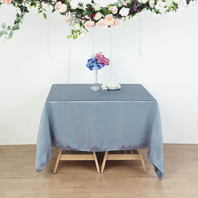 Gray satin tablecloth draped over a wooden table with floral decor above.