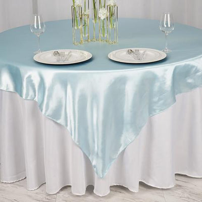 Round light blue satin tablecloth on a white table with plates and glassware.