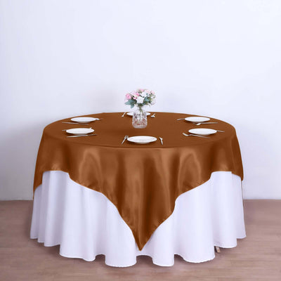 Brown satin tablecloth on a round table set with plates and a flower vase.