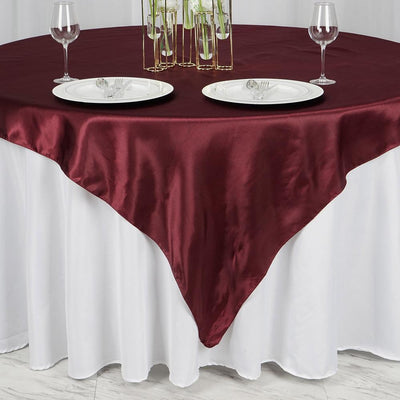 Burgundy satin tablecloth draped over a round table with elegant dinnerware.