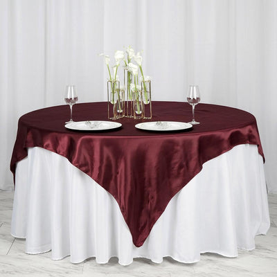 Elegant round table set with burgundy satin tablecloth and floral centerpiece.