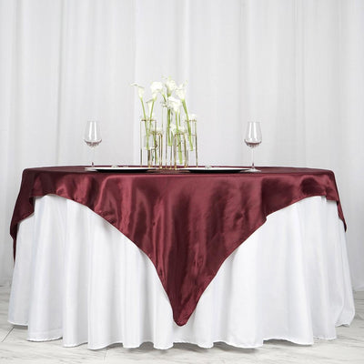 Elegant burgundy tablecloth draped over a white table with floral centerpiece and glassware.