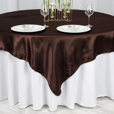 Brown satin tablecloth draped over a white table with plates and glasses.