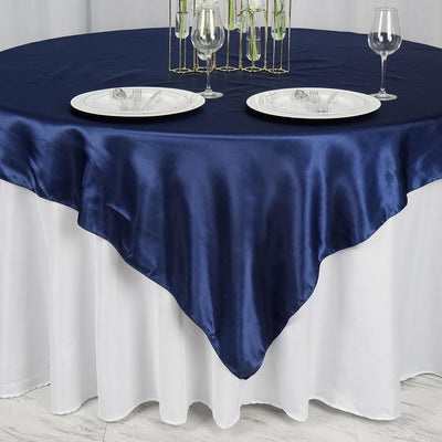 Navy satin tablecloth draped over a white table with plates and glasses.