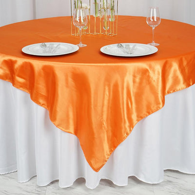 Orange satin tablecloth draped over a round table with plates and glasses.