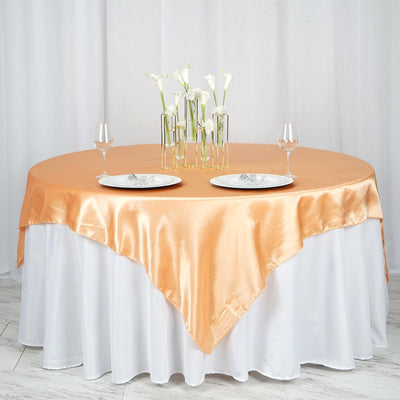 Round table set with an orange satin tablecloth and elegant glassware.