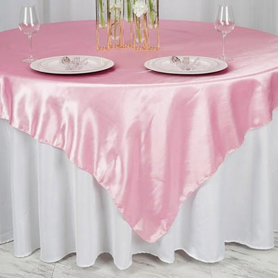 Pink satin tablecloth draped elegantly over a round table with plates and glasses.