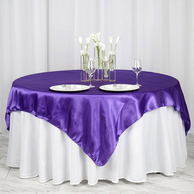 Purple satin tablecloth draped over a round table with elegant dinnerware.
