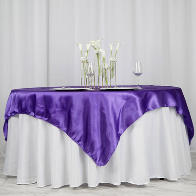 Purple satin tablecloth draped elegantly over a white table with floral centerpieces.