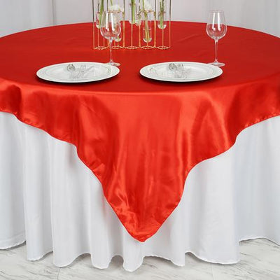 Red satin tablecloth draped over a round table set for dining.